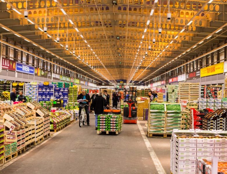 Photo du Marché de Rungis en pleine action. Il y a deux rangées de Fruits et Légumes. Des vendeurs sont dans l'allée centrale.